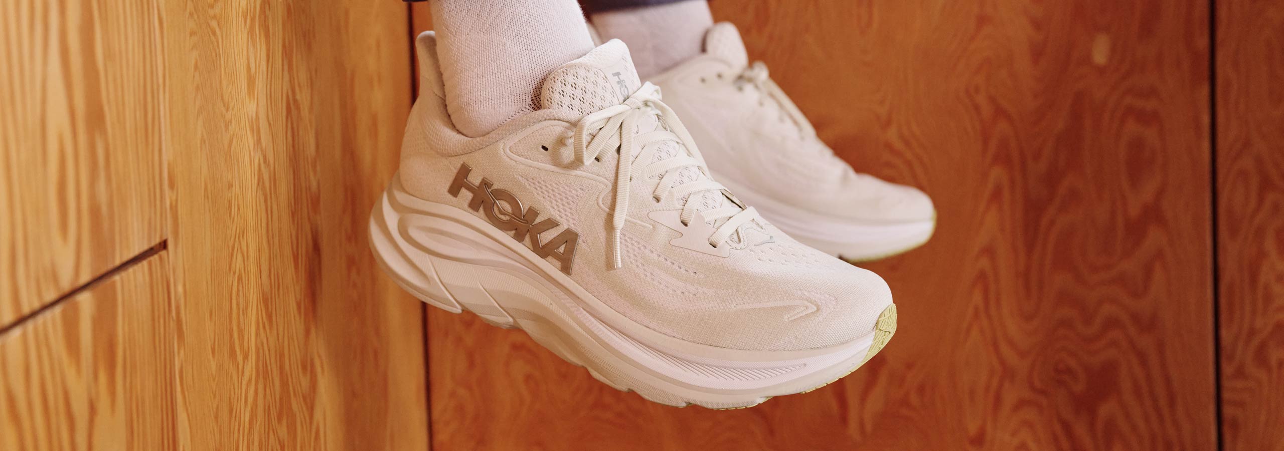 Beige Hoka sneakers on a wooden floor